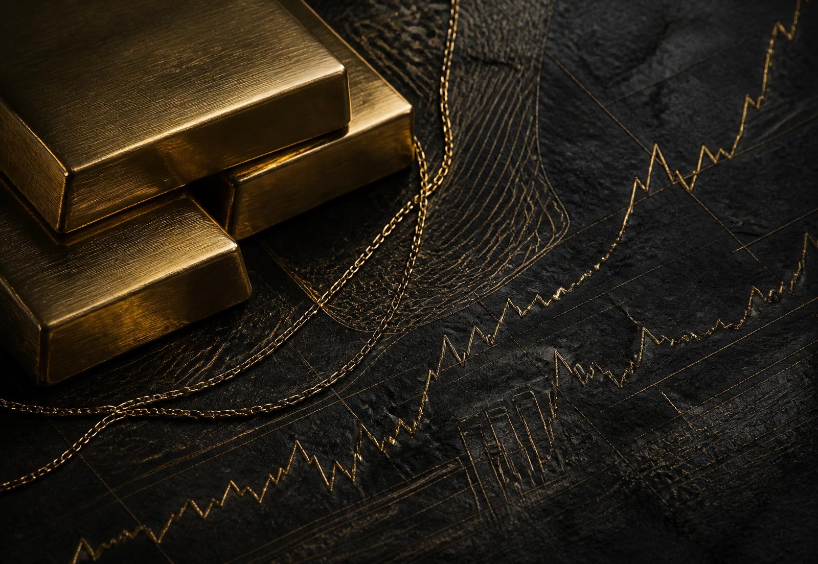 Gold bars and chain on dark stone with etched chart lines
